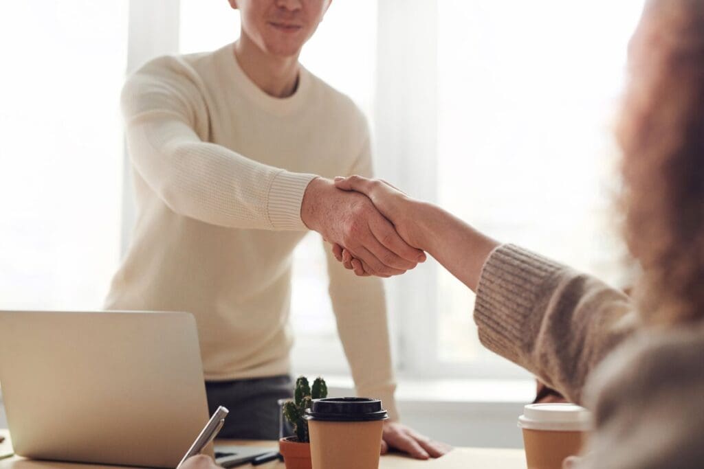 Two colleagues shaking hands across an office desk